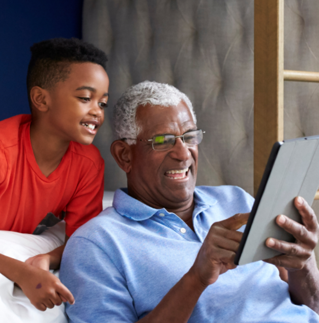Grandpa sitting on couch holding a tablet with grandson looking over